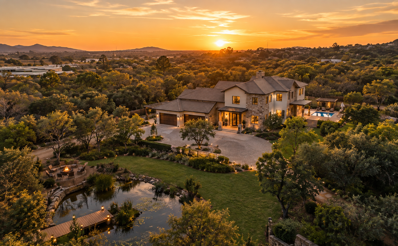 Aerial view at sunset of a large freestanding home with a swimming pool, pond, lawns and trees